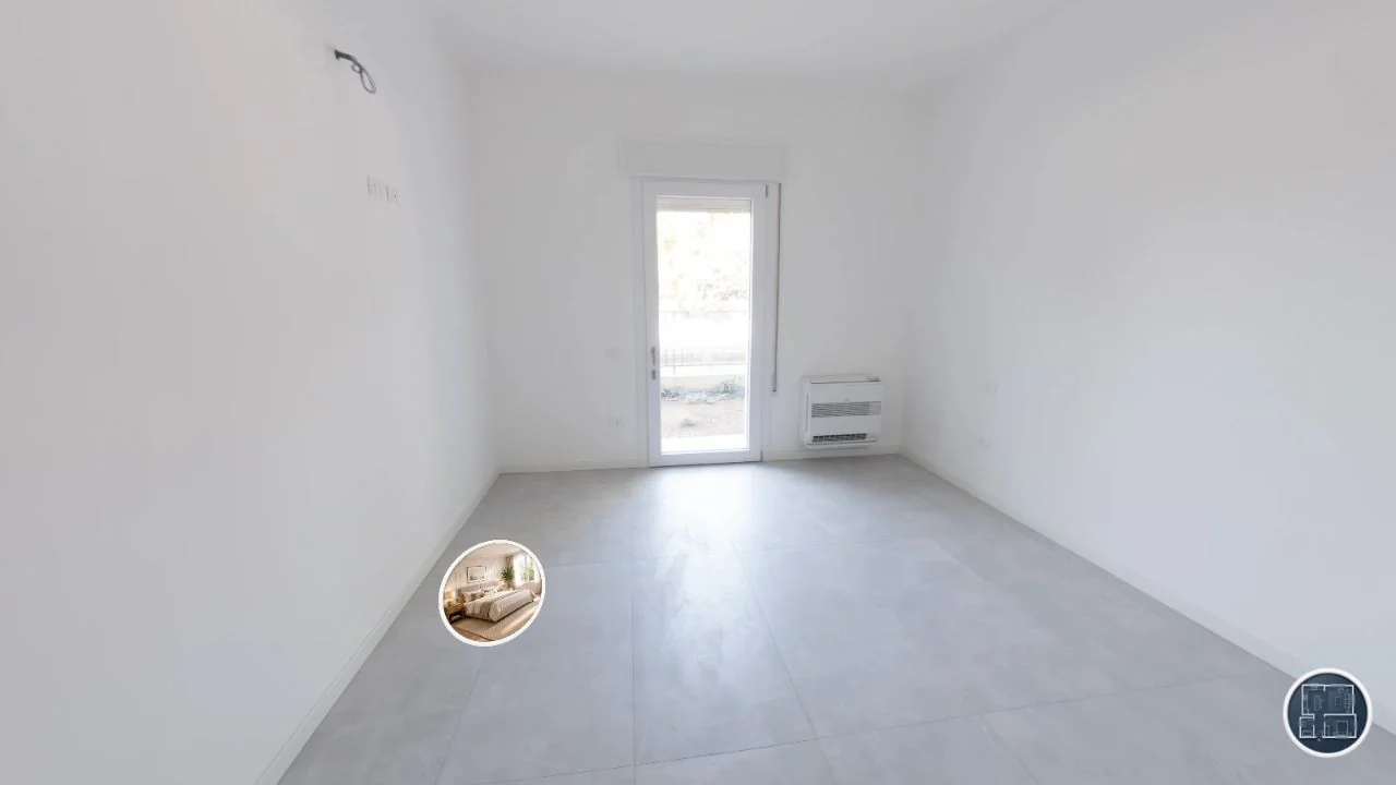 La camera da letto ristrutturata senza arredi: pareti bianche, pavimento nuovo, porta finestra e termosifone visibili